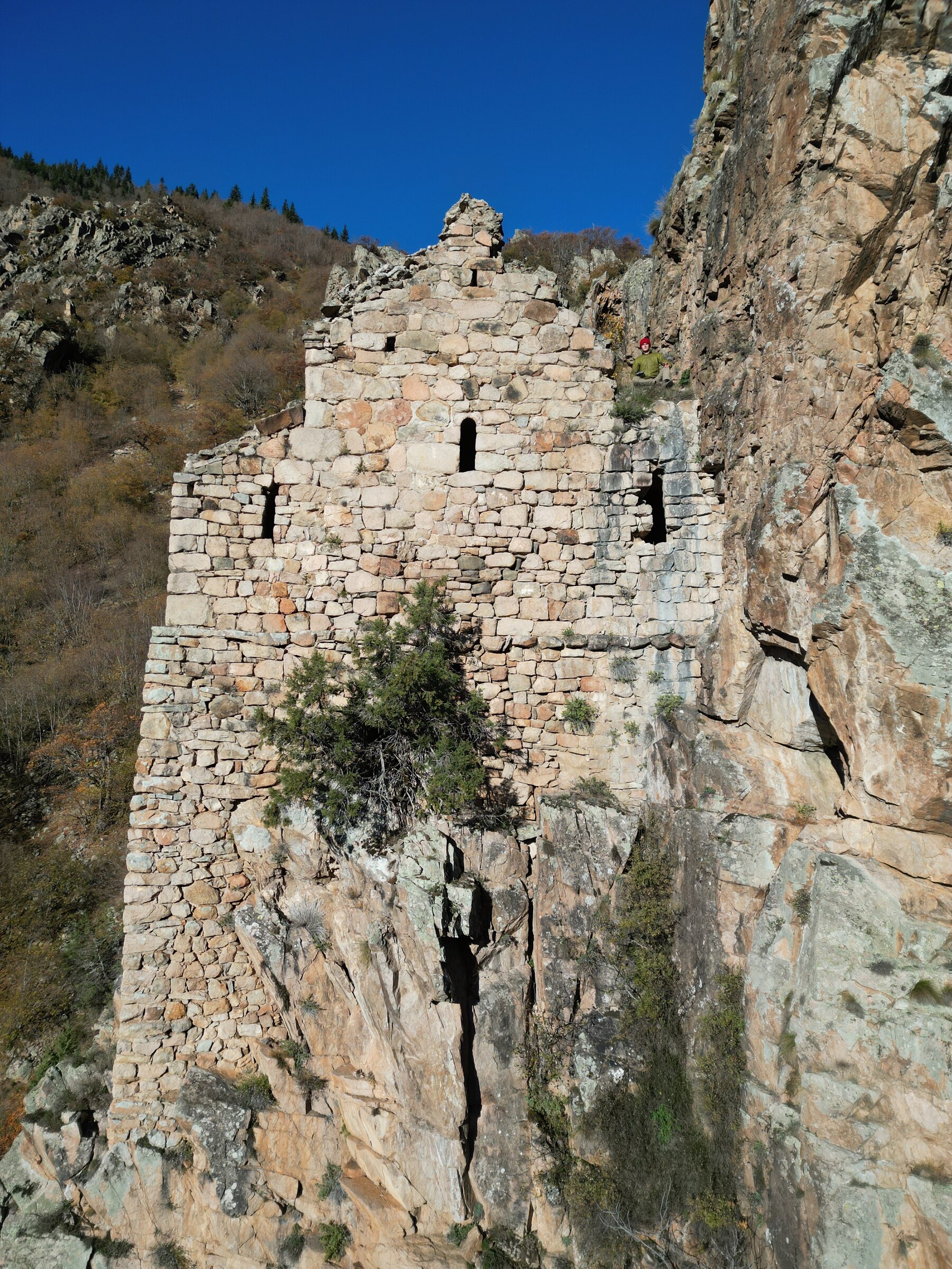 The wall with its narrow windows, rising from the rock